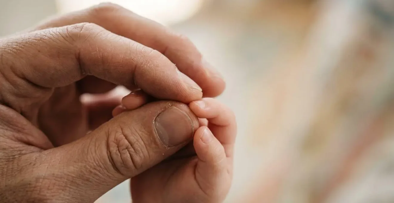 Gros plan sur les mains d'un parent tenant celles d'un jeune enfant, évoquant le soutien familial et la responsabilité parentale